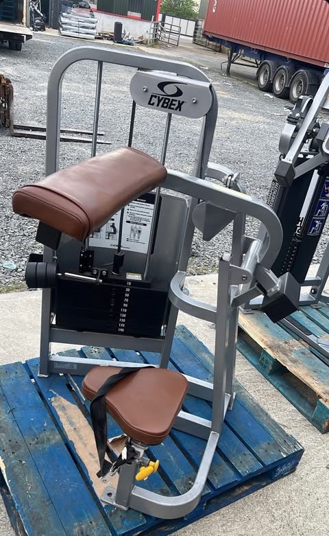A weight training machine with a brown seat and a black frame, placed on a blue wooden pallet.