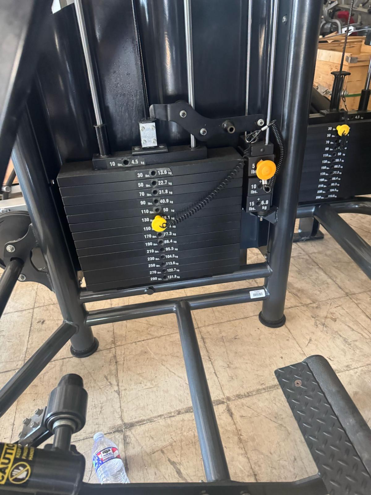 a weight training machine with a black metal frame and a black weight stack. The weight stack has various numbers and weights printed on it, indicating the different exercises and weights available for use.