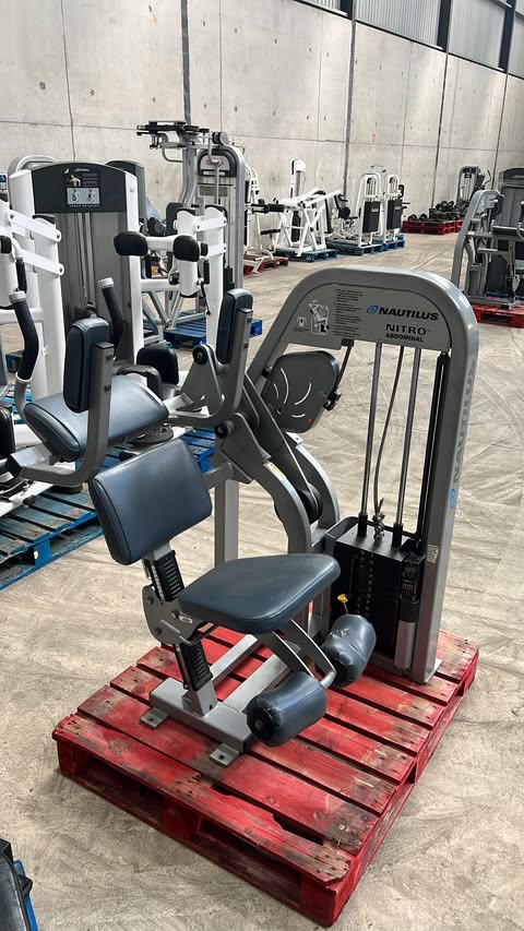 a weight training machine in a gym, with various other exercise equipment visible in the background.