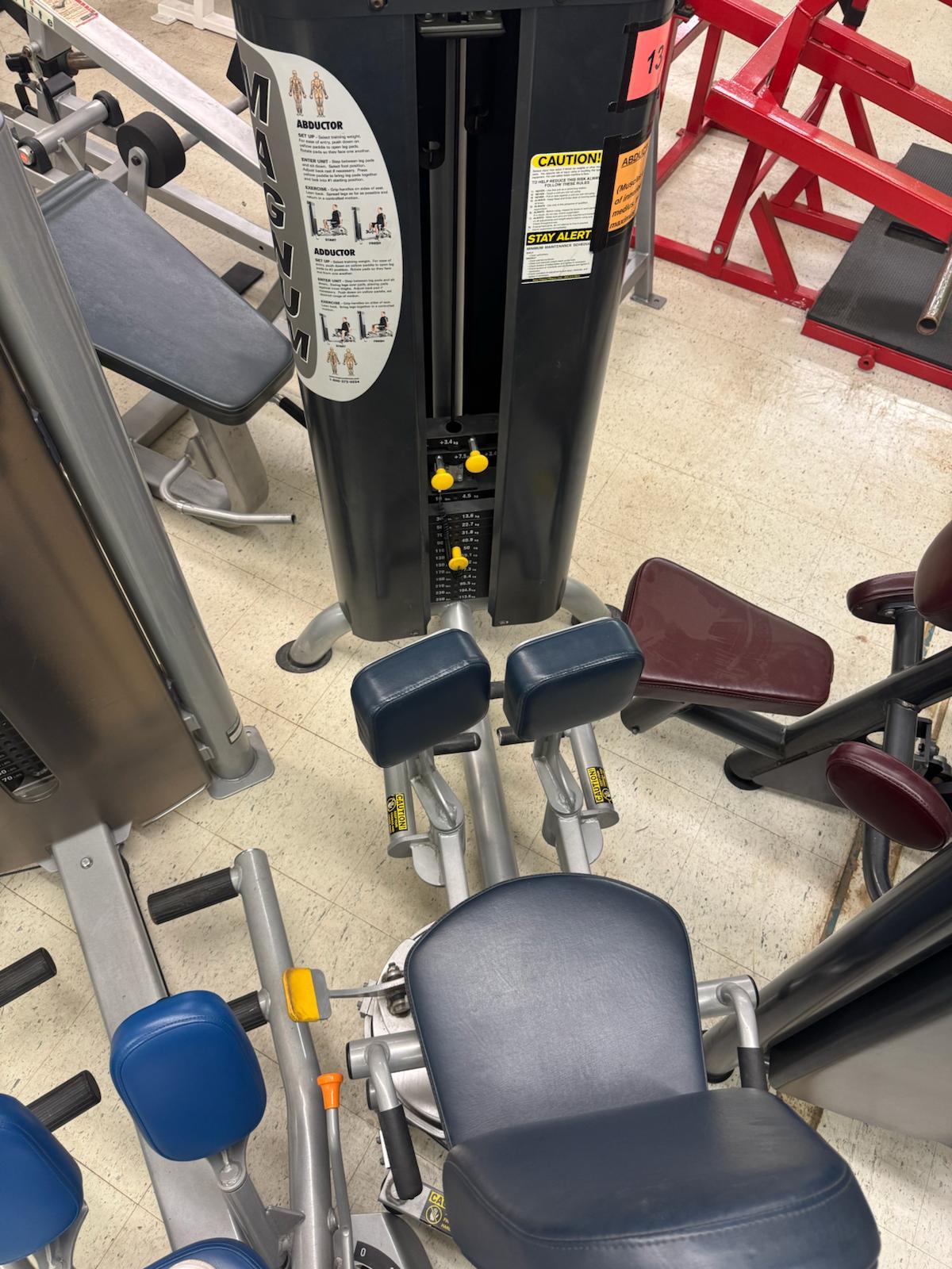a variety of exercise machines and equipment in a gym setting, including a large black machine with a yellow warning label.