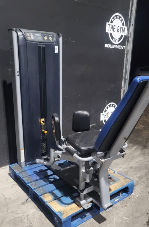 a weight training machine, specifically a leg press, placed on a blue pallet in front of a gym equipment store.