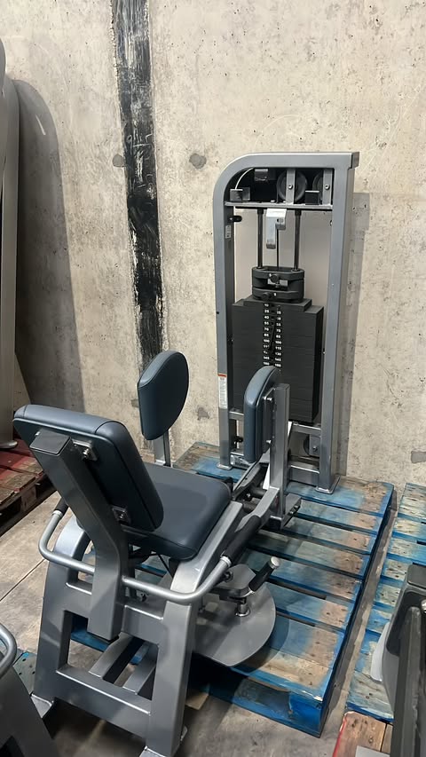a weight training machine with a black seat and a blue platform, situated in a room with a concrete wall.