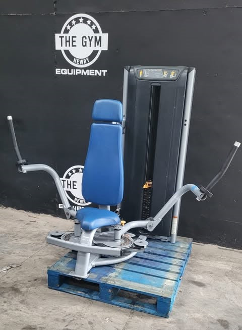 a blue and gray weight training machine, likely a dumbbell or weight machine, placed on a wooden pallet against a black wall with a logo for "THE GYM" and "WEIGHT EQUIPMENT".