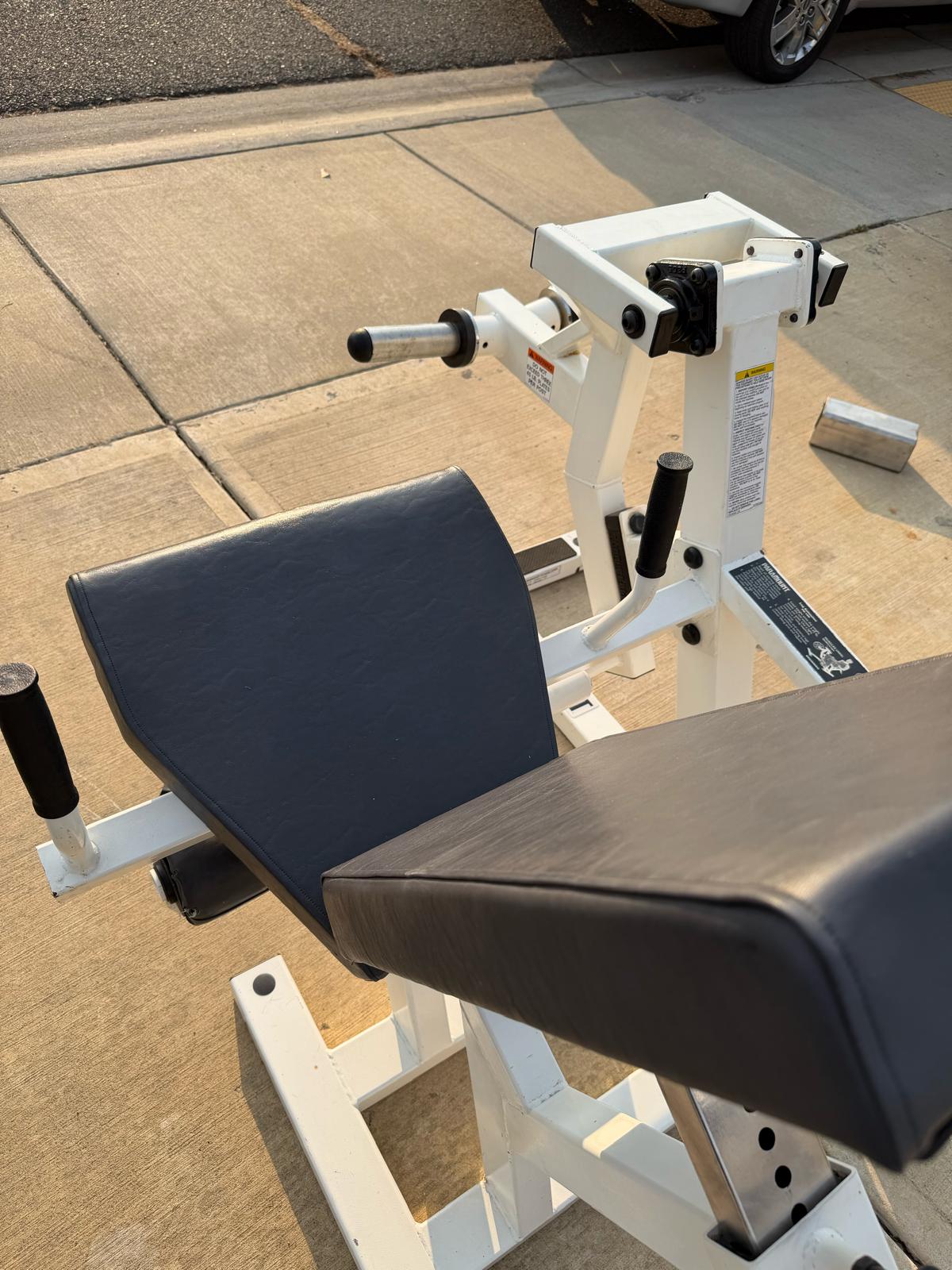 a weight training machine with a black seat and a white frame, positioned on a concrete surface.
