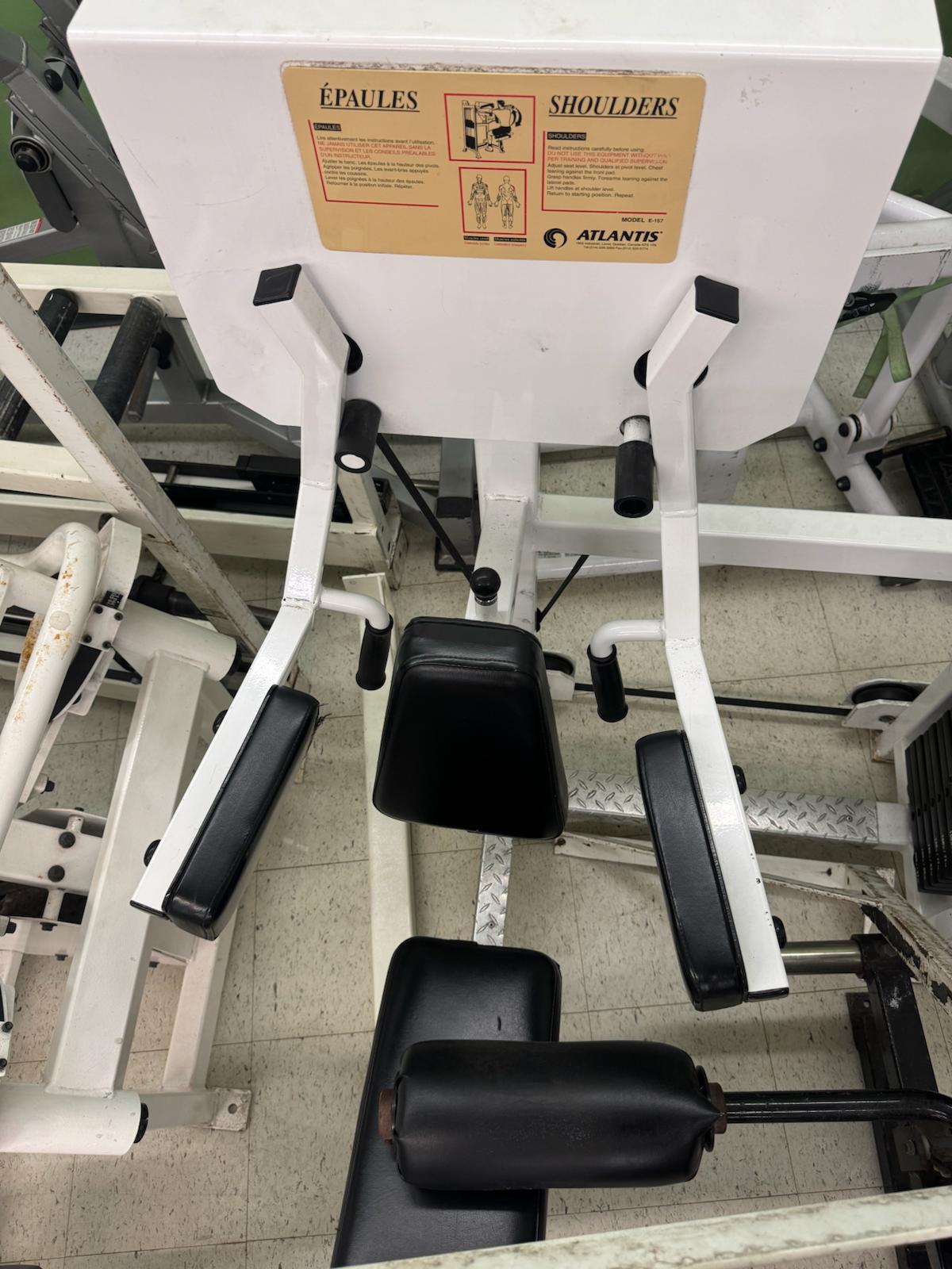 a weight training machine with various black and white components, including a barbell and weight plates. There is a yellow label on the machine that provides information about the machine's features and safety guidelines.