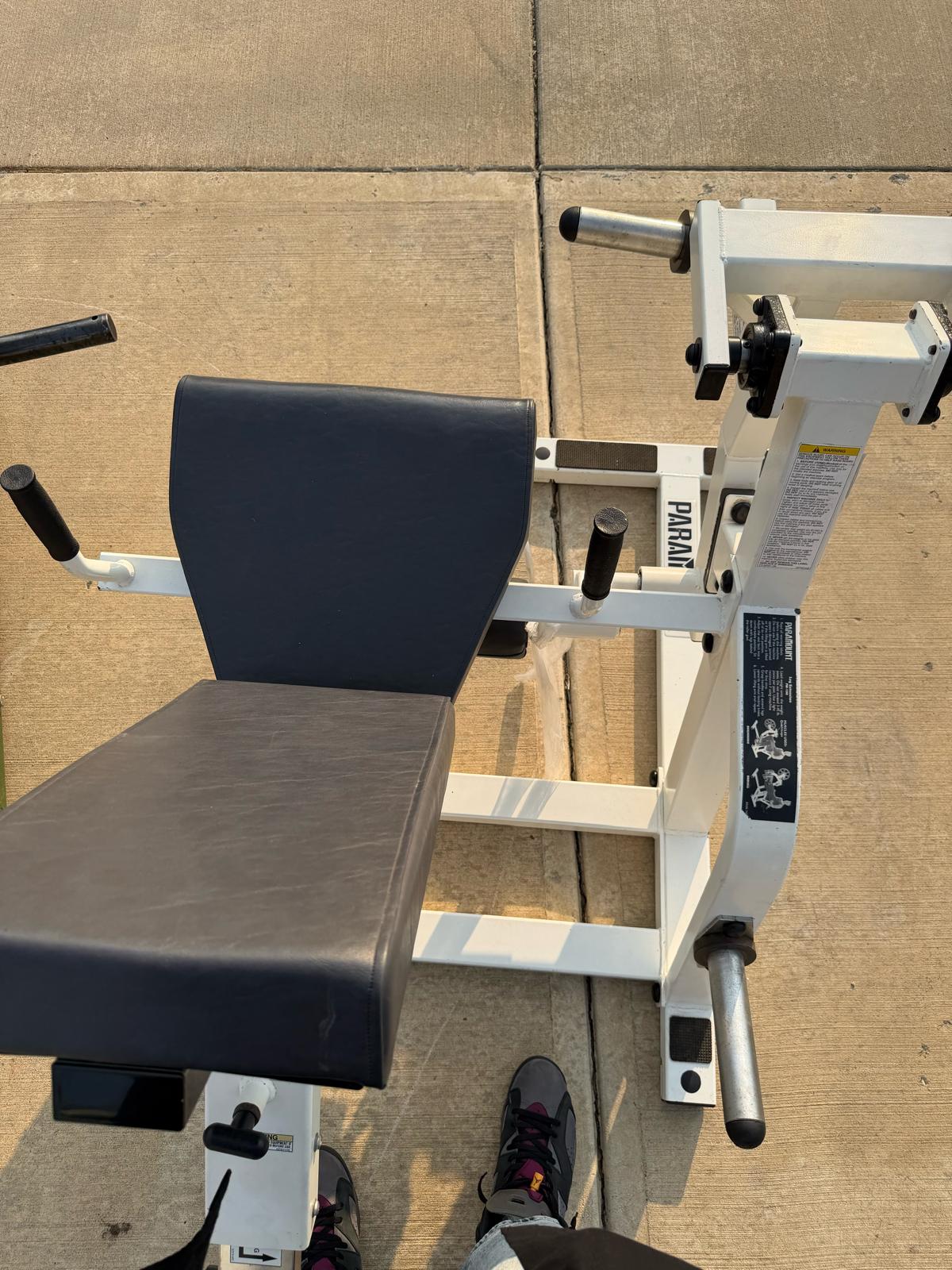 a weight training machine with a black seat and a white frame, placed on a concrete surface.
