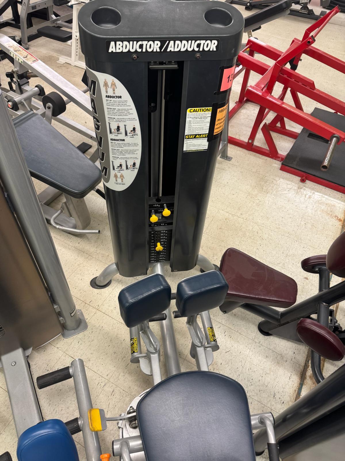 a gym with various exercise equipment, including a large black machine labeled "ABDUCTOR/ABDUCTOR" and several other machines in the background.