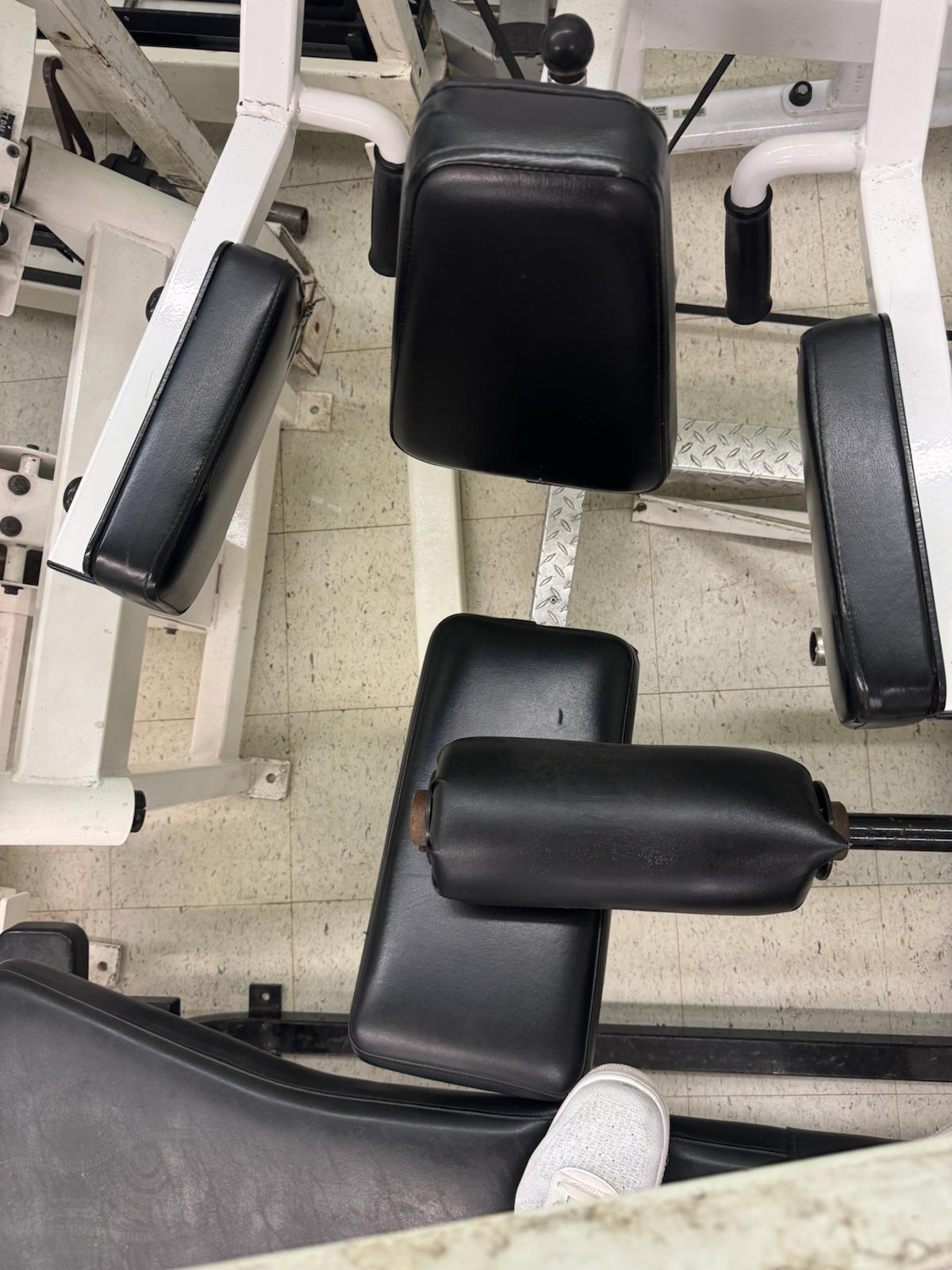 a gym setting with various exercise equipment, including black padded seats and a white exercise machine.