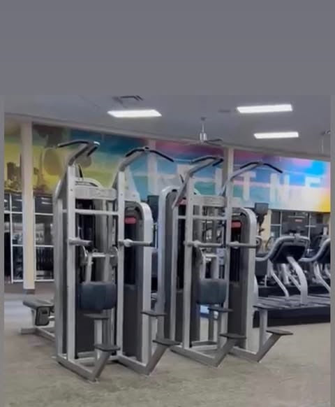 a well-equipped gym with various exercise machines, including a bench press and a leg press, arranged in a row.