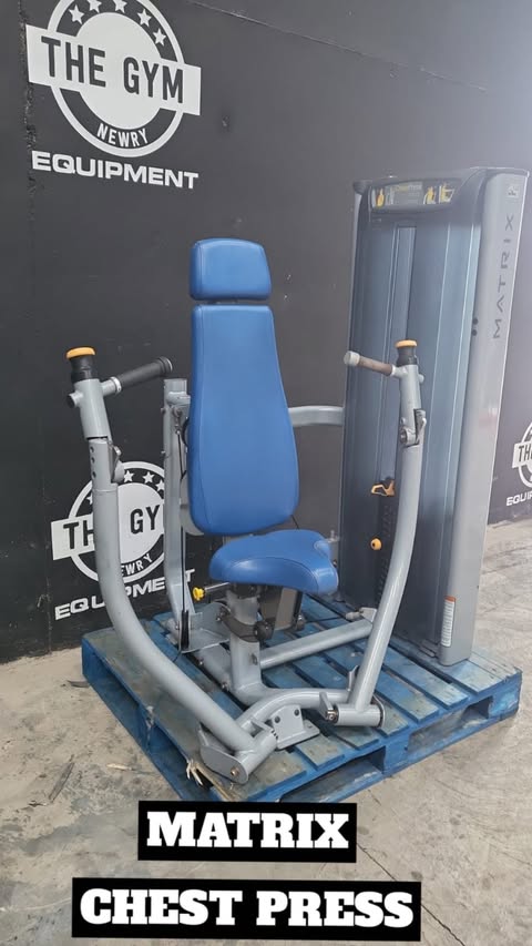A blue chest press machine is displayed in front of a gym equipment wall, with the text "MATRIX CHEST PRESS" visible.