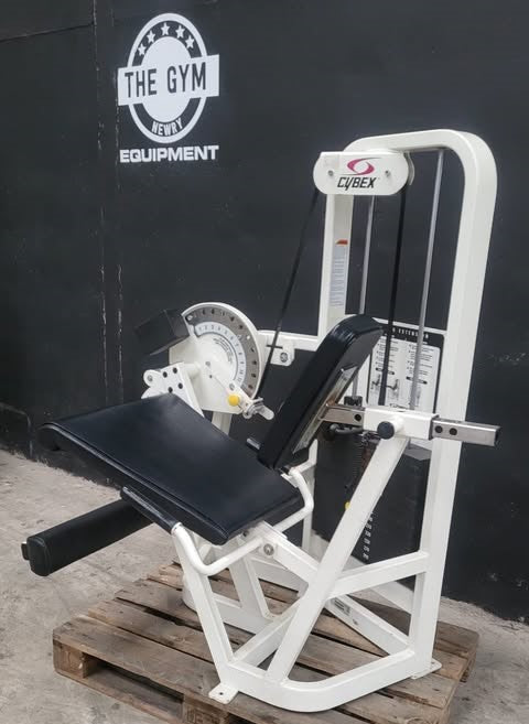 A weight training machine with a black seat and white frame is displayed against a black wall with a logo for "THE GYM" and "EQUIPMENT".