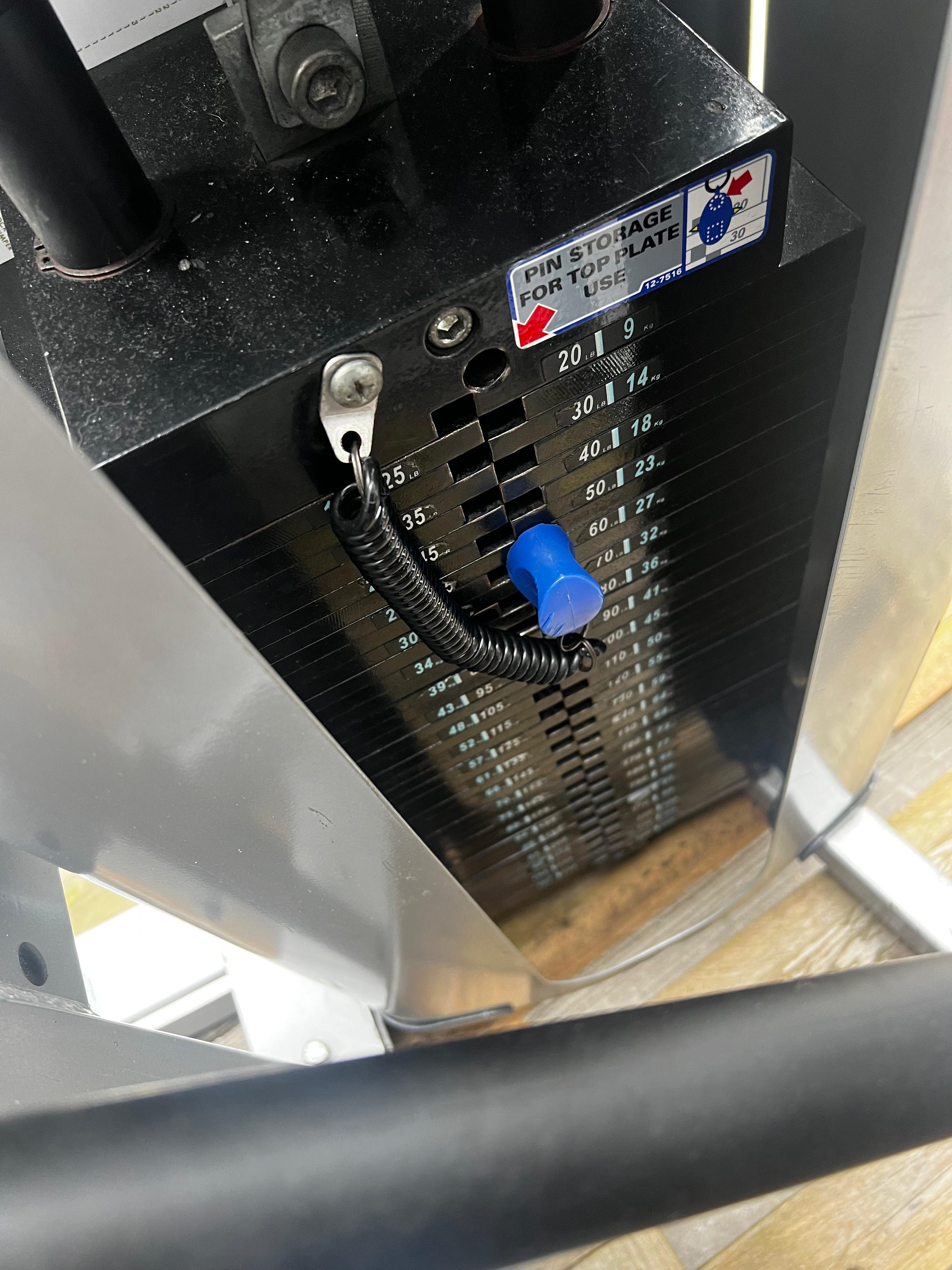 a close-up view of a weight training machine, specifically a weight plate with a blue cap attached to it. The weight plate has various numbers and measurements printed on it, indicating the weight it can hold.