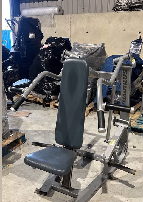 A weight training machine with a black seat and various pieces of equipment in the background.